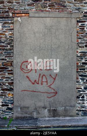 Cool image of a back street wall with a bricked up and rendered opening upon which someone has sprayed the words 'one way' with an arrow and a smile Stock Photo