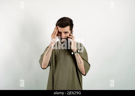 Handsome young man wearing casual clothes posing isolated over white background feeling upset desperate talking on the phone having problems. Hearing Stock Photo