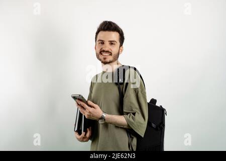 Cheerful caucasian man wearing casual clothes posing isolated over white background mobile phone and backpack with books. Looking at the camera. Stock Photo