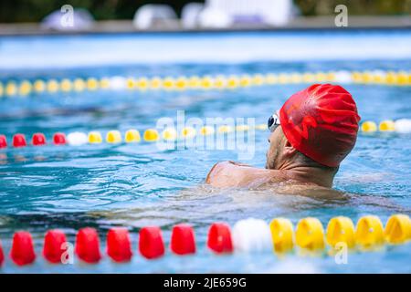 Live portrait of young sportive man, professional swimmer in goggles training at public swimming-pool, outdoors. Sport, power, energy, style, hobby Stock Photo