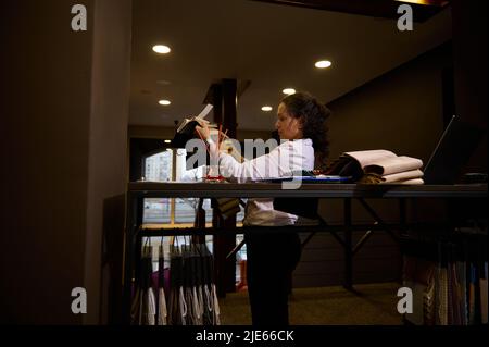 Inspired and creative woman freelance interior designer browsing colorful textiles for new home design project standing near a stand with upholstery f Stock Photo