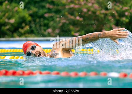 Live portrait of young sportive man, professional swimmer in goggles training at public swimming-pool, outdoors. Sport, power, energy, style, hobby Stock Photo