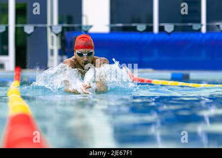 Live portrait of young sportive man, professional swimmer in goggles training at public swimming-pool, outdoors. Sport, power, energy, style, hobby Stock Photo