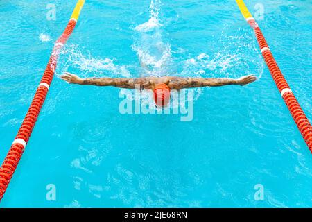 Live portrait of young sportive man, professional swimmer in goggles training at public swimming-pool, outdoors. Sport, power, energy, style, hobby Stock Photo