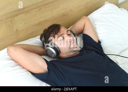 Young man relaxing on bed with headphones Stock Photo