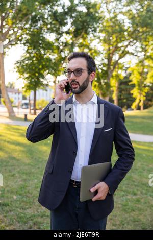 Businessman in the park answers his cell phone while walking to get away from the office. Stock Photo