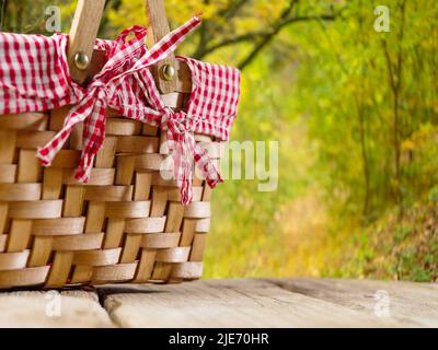 Against the background of beautiful summer nature, a picnic basket on a simple wooden table. Recreation, picnic, holiday, birthday in nature with frie Stock Photo