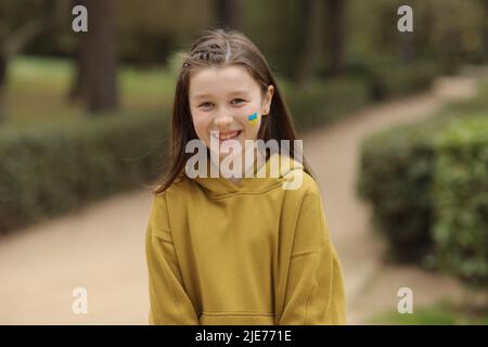 Smiling child girl with painted Ukrainian flag yellow and blue color on her cheek. Ukrainian children. flag symbols of Ukraine. Stock Photo