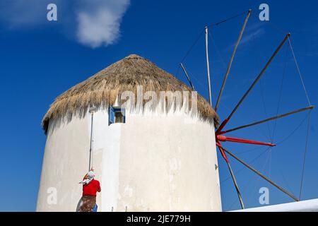 Mykonos, Greece - June 2022: Person painting the exterior wall of one of the famous windmills on the Greek island of Mykonos Stock Photo