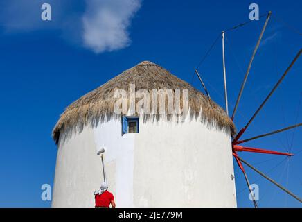 Mykonos, Greece - June 2022: Person painting the exterior wall of one of the famous windmills on the Greek island of Mykonos Stock Photo