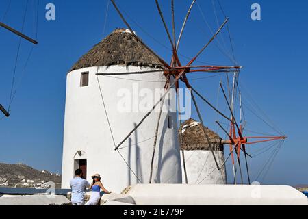 Mykonos, Greece - June 2022: Person posing for a photograph in front of one of the famous windmills on the Greek island of Mykonos Stock Photo
