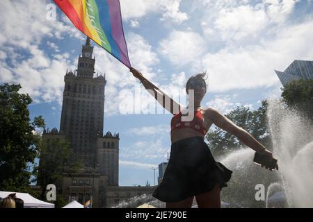 Warsaw, Poland. 25th June, 2022. A woman waving the rainbow flag stands near the fountain and with the Palace of Culture and Science in the background as she participates in the Warsaw Equality Parade. The parade was organised to promote social equality and draw attention to the problems faced by the LGBT community in Poland. This year the Warsaw Equality Parade hosted the Kyiv Pride - largest Ukraine's LGBTQ rights parade. As well as LGBTQ and equality slogans, participants showed their support against the war and Russia's invasions of Ukraine. Credit: SOPA Images Limited/Alamy Live News Stock Photo