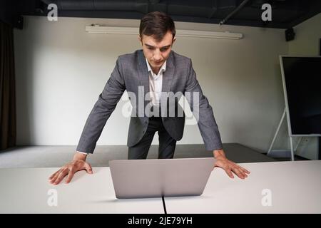 Serious man leaning over laptop on table in office Stock Photo