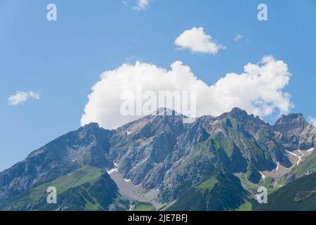 Landscape shot of a large karstic rocky partly grassy mountain massif in the Austrian Tyrolean Alps with last remnants of snow against blue sky and wh Stock Photo