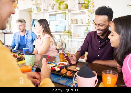 Man and woman watching something in a cell phone. Group of people using phone smiling in a cafe bar. Friends having breakfast and community concept Stock Photo