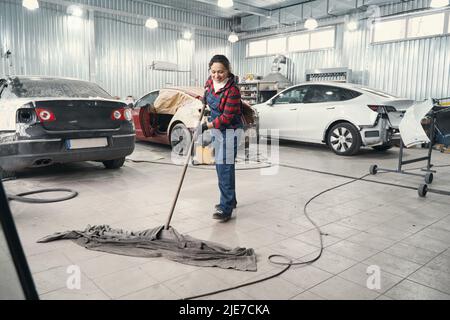 Delighted female person cleaning floor in the workshop Stock Photo