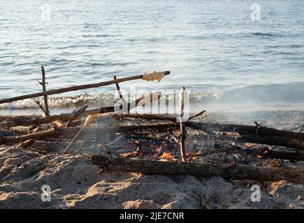 Stick bread cooked on campfire. Bread dough twisted on wooden stick and roasted on fire. Fun camping food for kids. Beach picnic grill or barbeque. Stock Photo