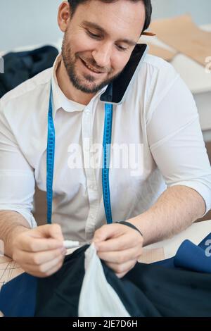 Cheerful male dressmaker talking on smartphone in workshop Stock Photo