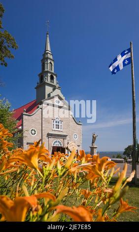 Saint-Jean church through orange Hemerocallis - Daylilies daylilies in summer, Saint-Jean, Ile d'Orleans, Quebec, Canada. Stock Photo