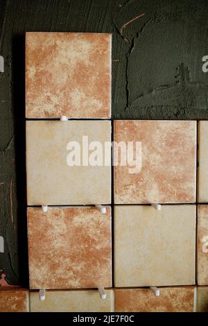 A section of freshly laid brown and cream tiles on the wall with plastic gaskets. Repair work. Stock Photo
