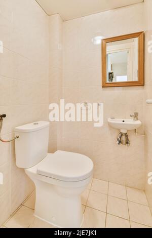 Modern flush toilet and ceramic sink mounted on beige tiled walls next to a mirror in a small closet at home Stock Photo