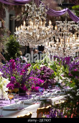 Beautiful crystal chandeliers with bulbs above laid celebration table with tableware for ceremony. Stock Photo