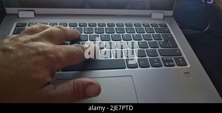 hand of a person typing on a gray pc with white letters Stock Photo