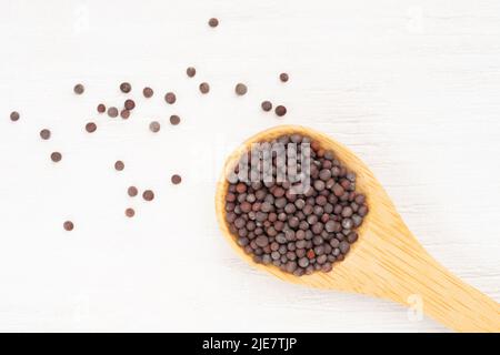 Mustard seeds in wooden spoon and scattered on white wooden background. Close up. Vegetarian food concept Stock Photo
