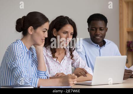 Three multiracial employees use laptop discuss online presentation Stock Photo