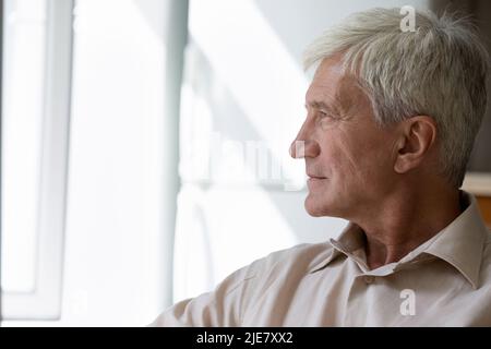 Side profile view pensive older man sit staring out window Stock Photo