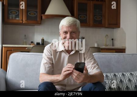 Mature man sit on couch with smartphone looking at camera Stock Photo