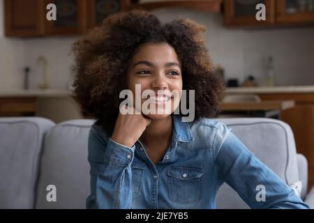 Beautiful African curly-haired girl seated on couch staring aside Stock Photo