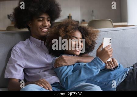 Teenage couple relax on sofa having fun using smart phone Stock Photo
