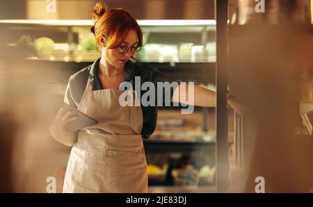 Young supermarket owner taking inventory using a digital tablet in her shop. Young female entrepreneur running her small business using wireless techn Stock Photo