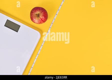 Dieting concept with scale, measuring tape and apple on yellow background with copy space Stock Photo
