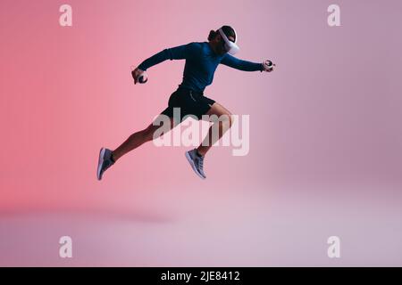 Athletic young man running mid air while wearing virtual reality goggles. Active young man working out in the metaverse. Sporty young man exploring a Stock Photo