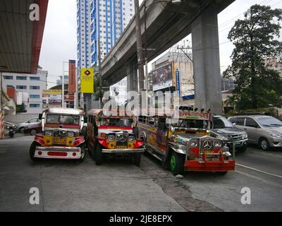 Jeepneys parked on the forecourt of a petrol station with metro train flyover overhead in Quezon city, Stock Photo