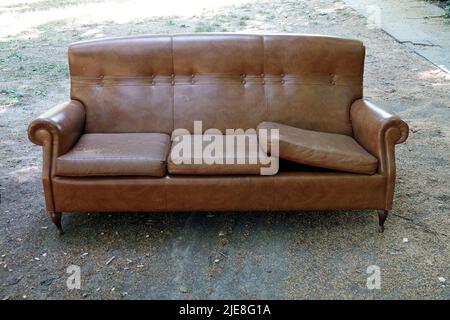 Old vintage brown leather sofa abandoned in a park Stock Photo