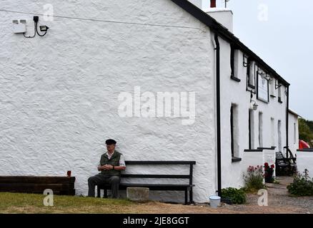 Man sitting with drink outside the Old Point House pub, Angle, Pembrokeshire, Wales Stock Photo