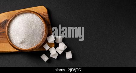 Granulated sugar and sugar cubes in wooden bowl on dark background Stock Photo