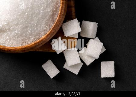 Granulated sugar and sugar cubes in wooden bowl on dark background Stock Photo