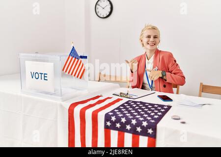 Beautiful caucasian woman working at political campaign pointing to the back behind with hand and thumbs up, smiling confident Stock Photo