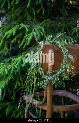 wild meadow flower wreath in the summer garden on the edge of a wooden chair. Summer solstice day, Midsummer concept. traditional floral decor. pagan Stock Photo