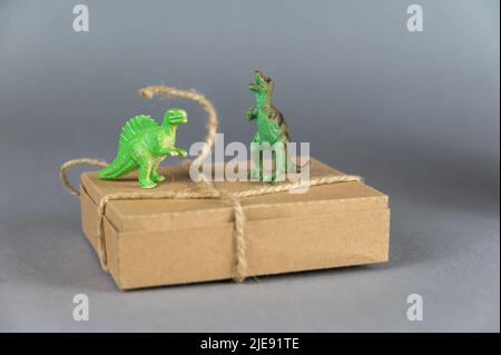 Brown cardboard box and miniatures of two dinosaurs against a gray background. Small green figures of animals of prey standing on their hind legs. Rec Stock Photo