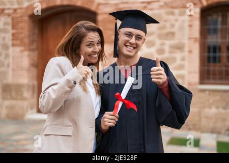 Man and woman mother and son doing ok gesture holding graduate diploma at university Stock Photo
