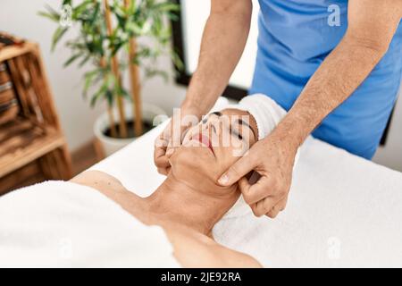 Middle age man and woman wearing therapist uniform having facial massage session at beauty center Stock Photo