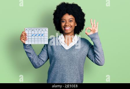 Young african american woman holding travel calendar doing ok sign with fingers, smiling friendly gesturing excellent symbol Stock Photo