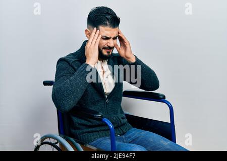 Handsome man with beard sitting on wheelchair with hand on head for pain in head because stress. suffering migraine. Stock Photo