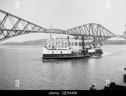 1956, historical view from this era of the Robert The Bruce ferry on the water beside the Forth Bridge, the world's first major steel structure. A cantilever railway bridge across the Firth of Forth in East of Scotland, near Edinburgh, its opening in 1890 was a major milstone in modern railway civil engineering and is the world's longest cantilever bridge. The ferry, Robert The Bruce, was built in 1934 by Clyde shipbuilders, William Denny, and could carry 500 passengers and 28 cars. It stopped operating in 1964 when the Forth Road Bridge opened. Stock Photo