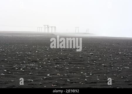 Diamond beach, black sand beach with electricity pylons in the background on a misty day. Iceland Stock Photo